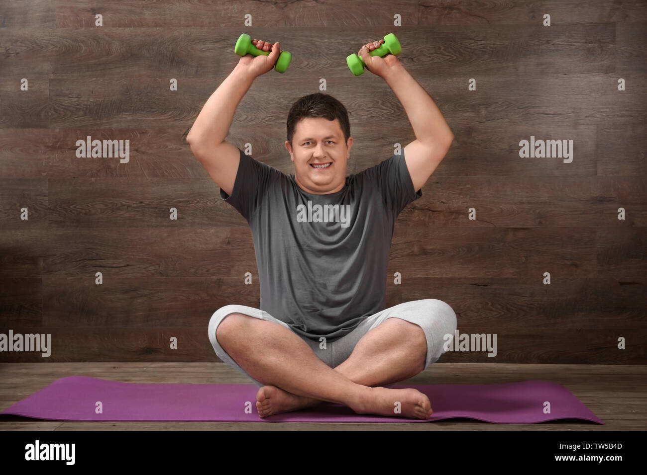 Overweight man training with dumbbells against wooden wall Stock Photo
