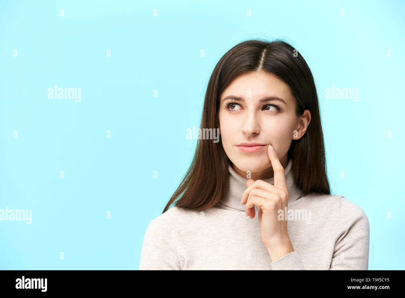 beautiful young caucasian woman looking up and contemplating, finger on lip, isolated on blue background Stock Photo