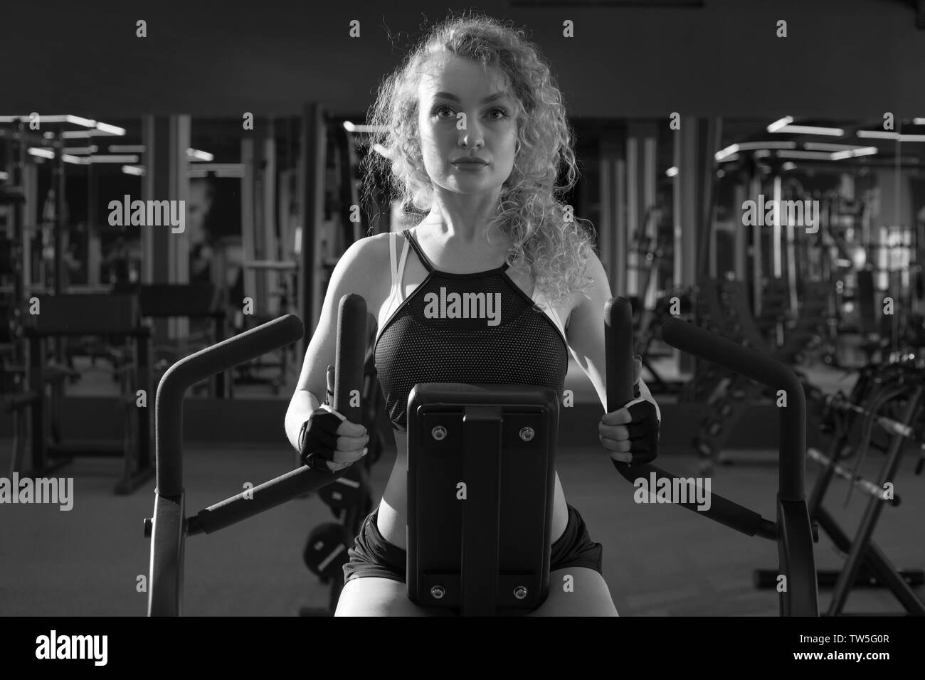 The girl is engaged in a rowing simulator in the gym. Stock Photo