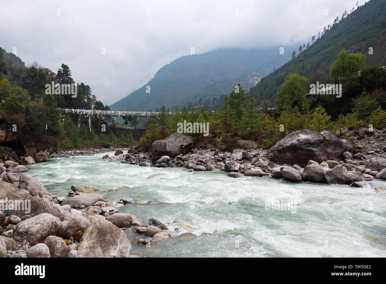 Suspension bridge draped with flags over rapid river in mountainous Nepal Stock Photo