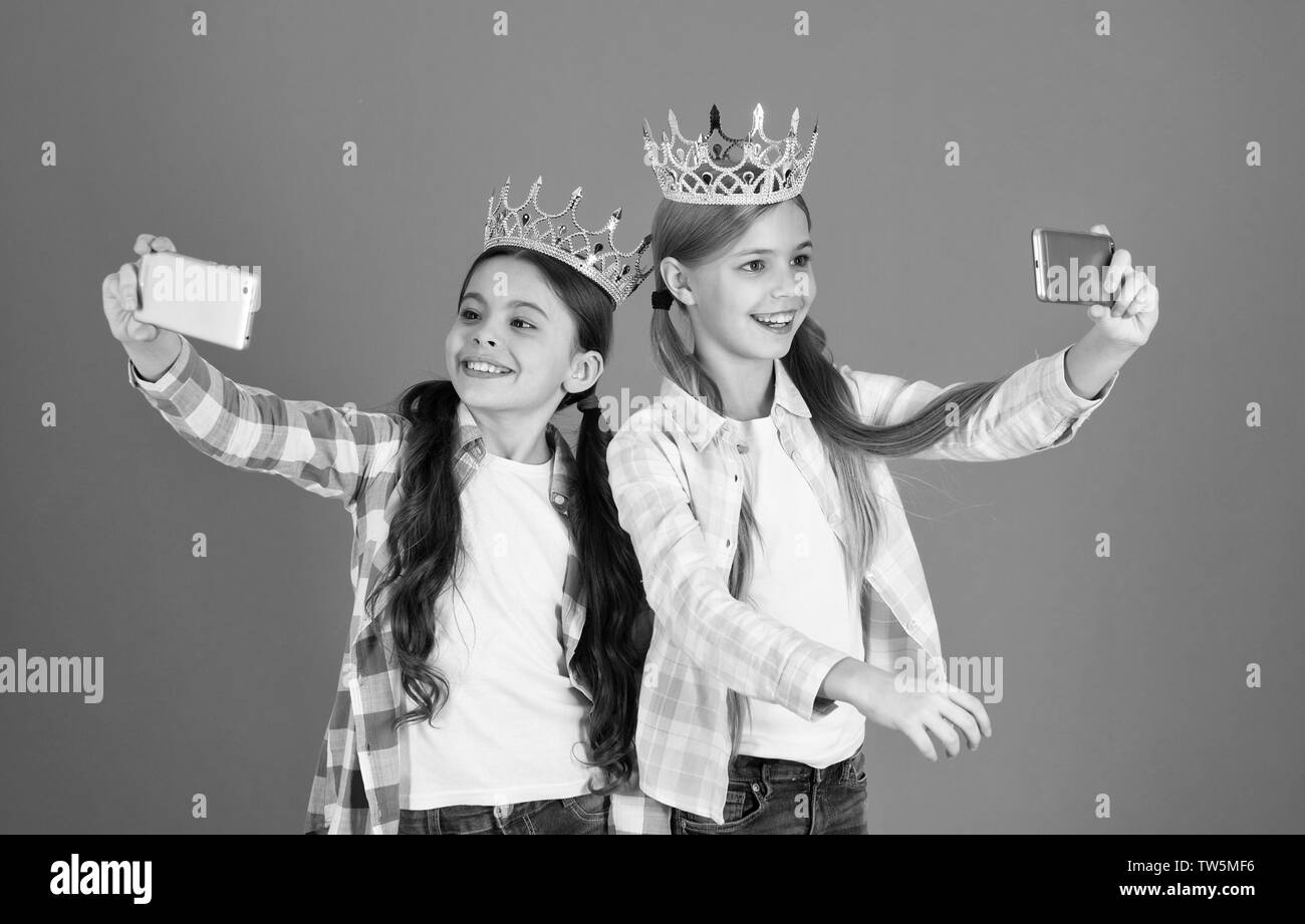 Girls taking selfie photo smartphone camera. Spoiled children concept. Egocentric princess. Kids wear golden crowns symbol princess. Warning signs of spoiled child. Avoid raising spoiled kids. Stock Photo