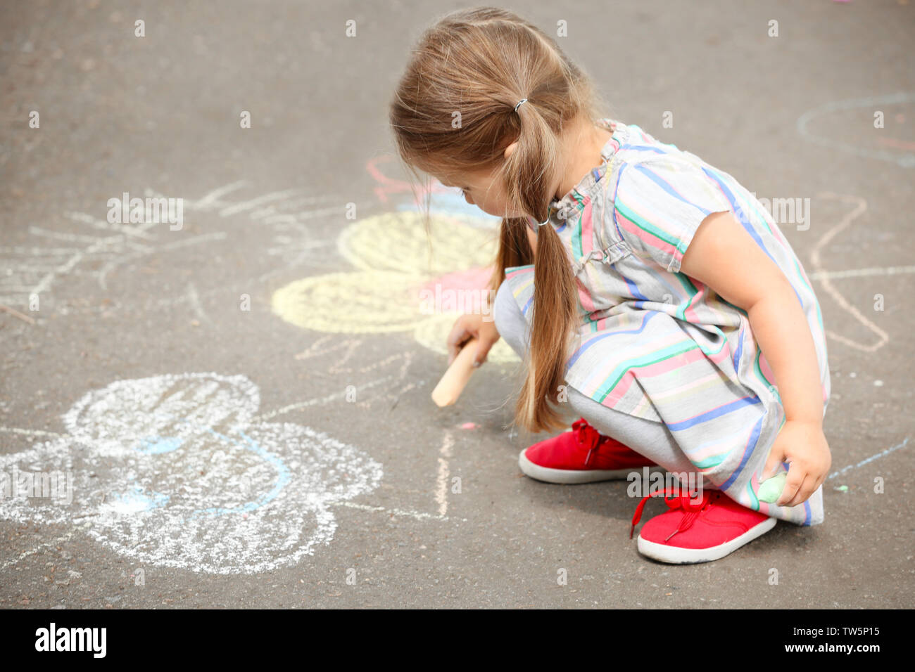 Cute little girl drawing with chalk on asphalt Stock Photo - Alamy