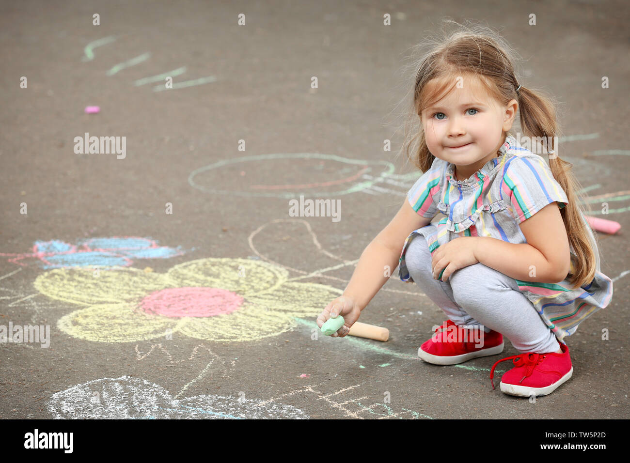 Cute little girl drawing with chalk on asphalt Stock Photo - Alamy