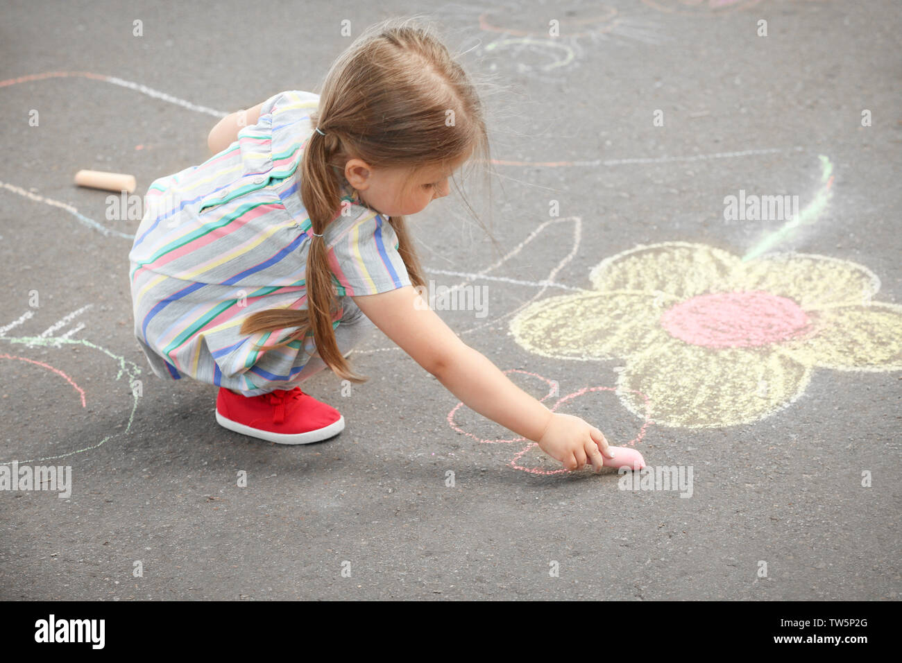 Cute little girl drawing with chalk on asphalt Stock Photo - Alamy