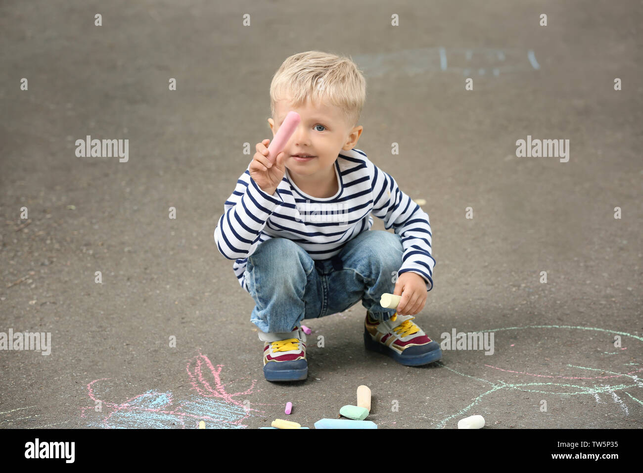 Cute little boy drawing with chalk on asphalt Stock Photo - Alamy