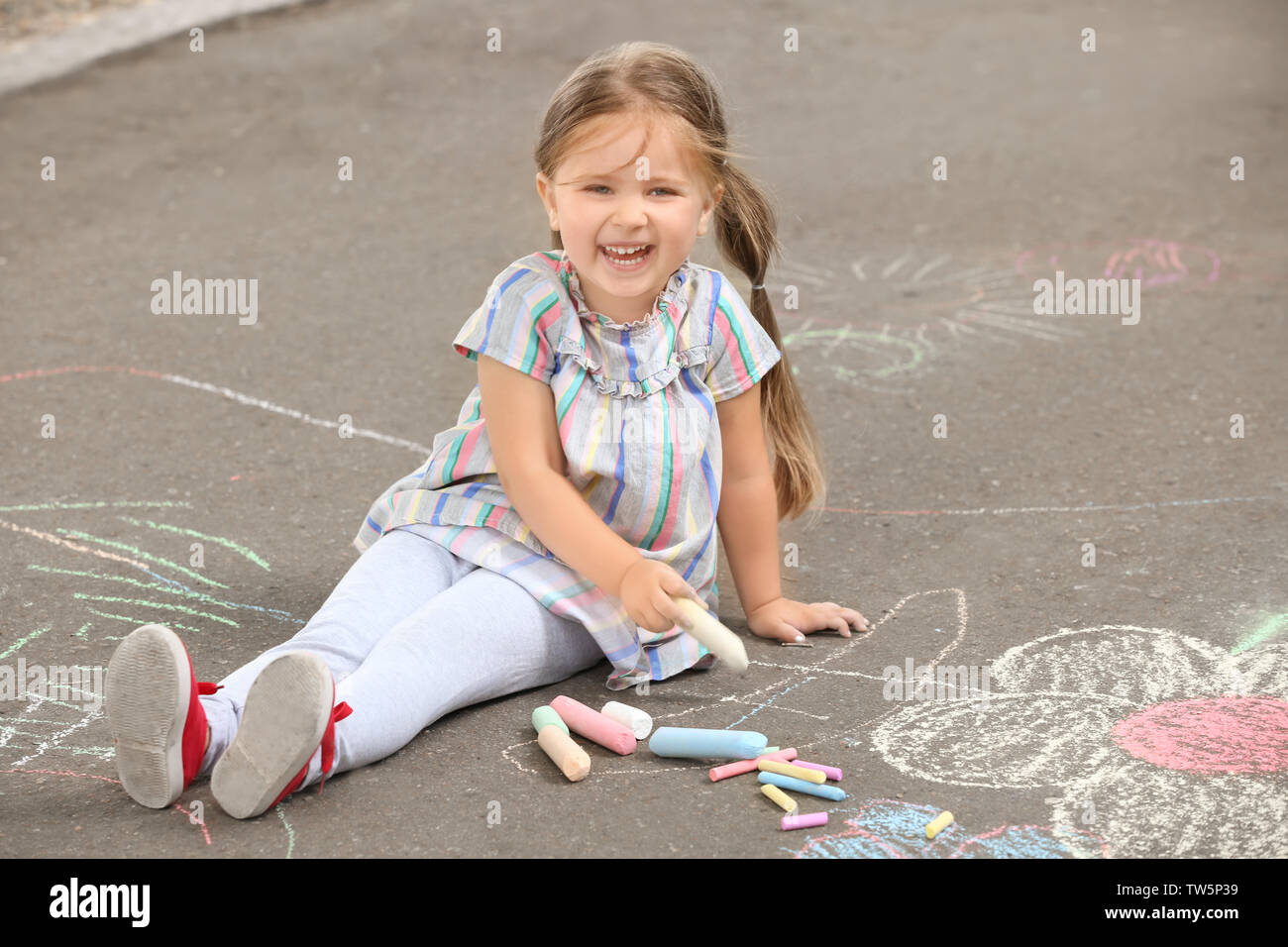 Cute little girl drawing with chalk on asphalt Stock Photo - Alamy