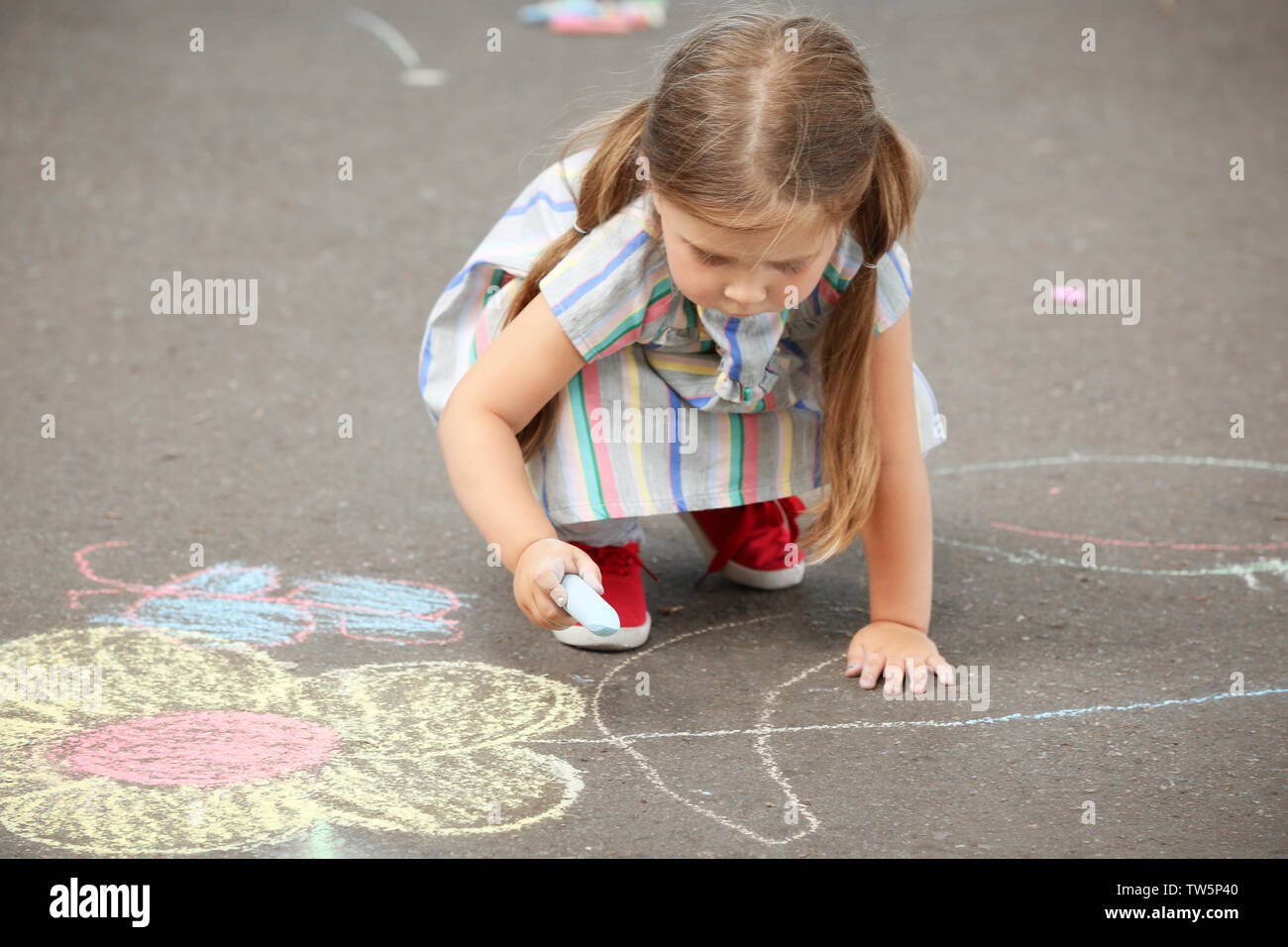 Cute little girl drawing with chalk on asphalt Stock Photo - Alamy