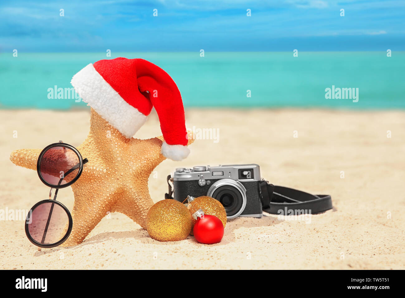Santa hat with sea star, camera and sunglasses on beach. Christmas ...