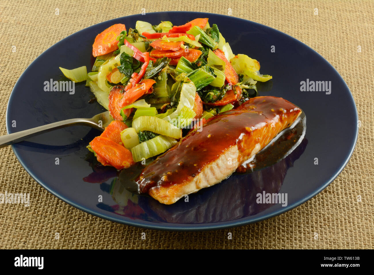 Baked salmon fish fillet with teriyaki sauce and vegetables on blue plate with fork Stock Photo