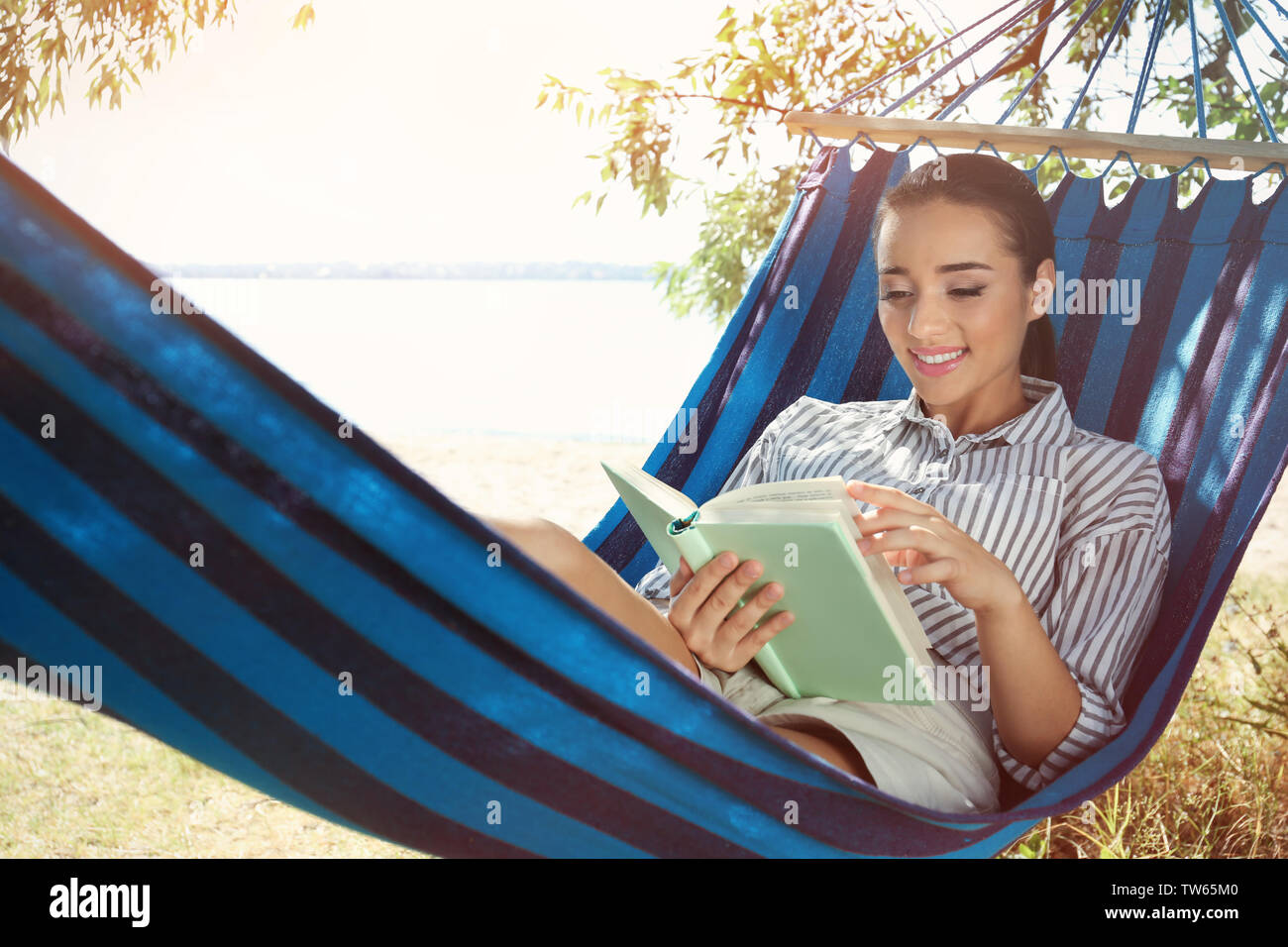 Young woman lying in hammock and reading book outdoors Stock Photo - Alamy