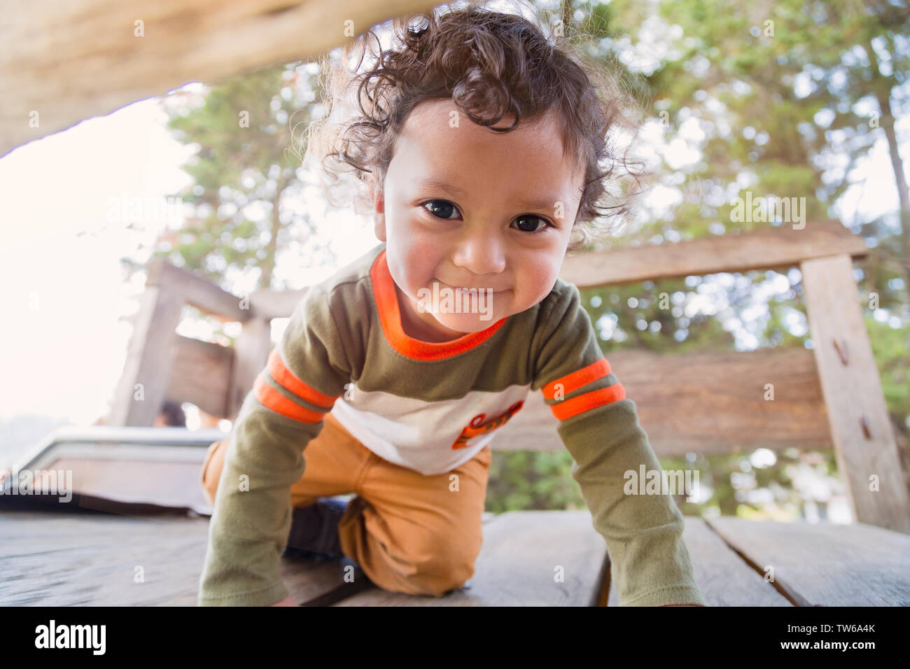 Cute child with big eyes crawling in a wooden game in the woods with the sun behind Stock Photo