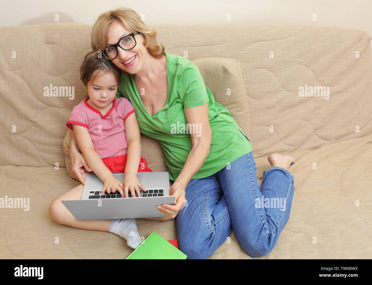 Cute girl and grandmother with laptop on sofa at home Stock Photo - Alamy