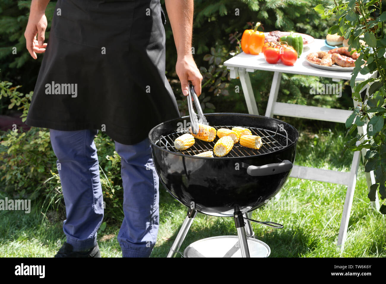 Man preparing delicious corn on barbecue grill outdoors Stock Photo