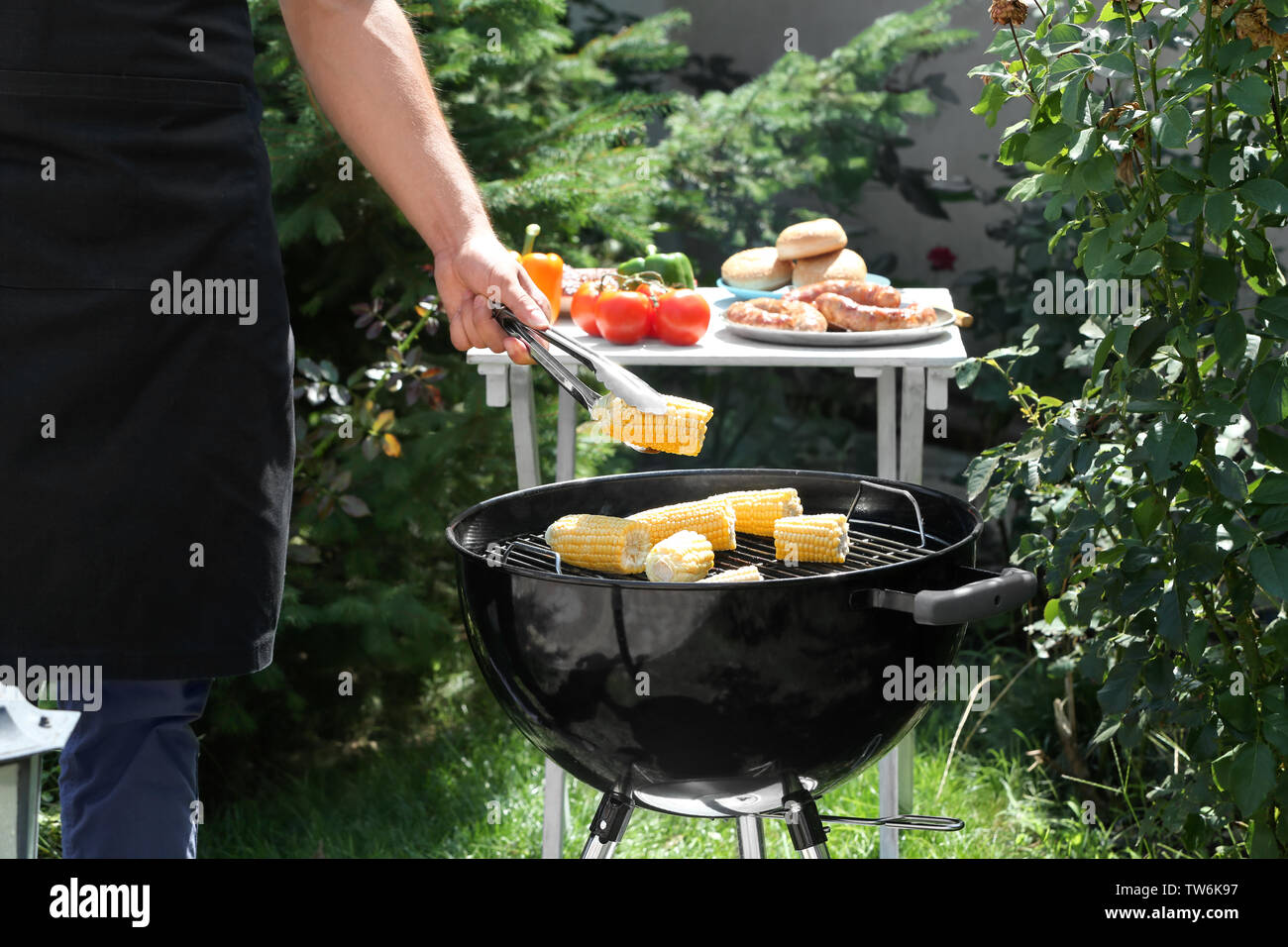 Man preparing delicious corn on barbecue grill outdoors Stock Photo