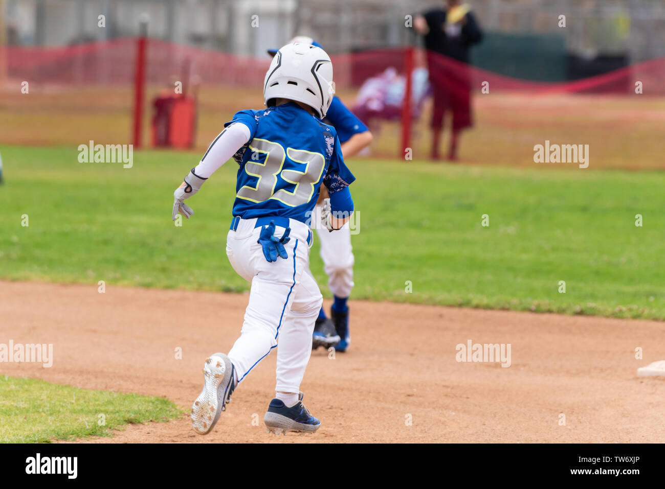 Youth baseball player in blue uniform and white helmet sprints across infield to steal second base. Stock Photo