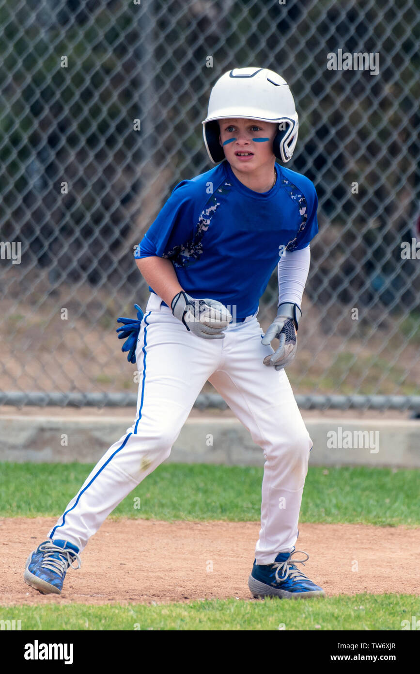 Youth baseball player in blue uniform and white helmet anticipating the right time to run. Stock Photo