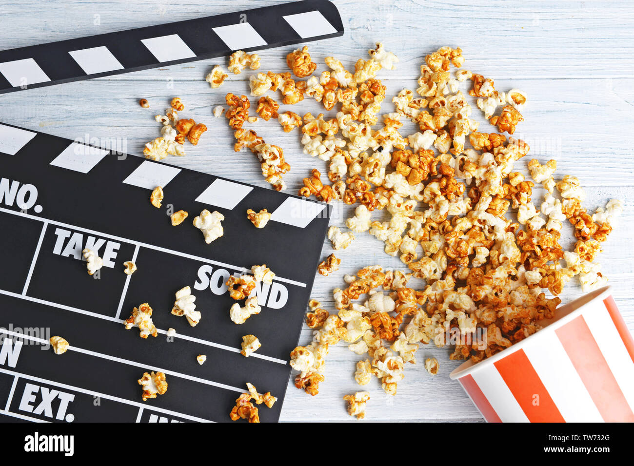 Paper cup with caramel popcorn and movie clapper on wooden background ...