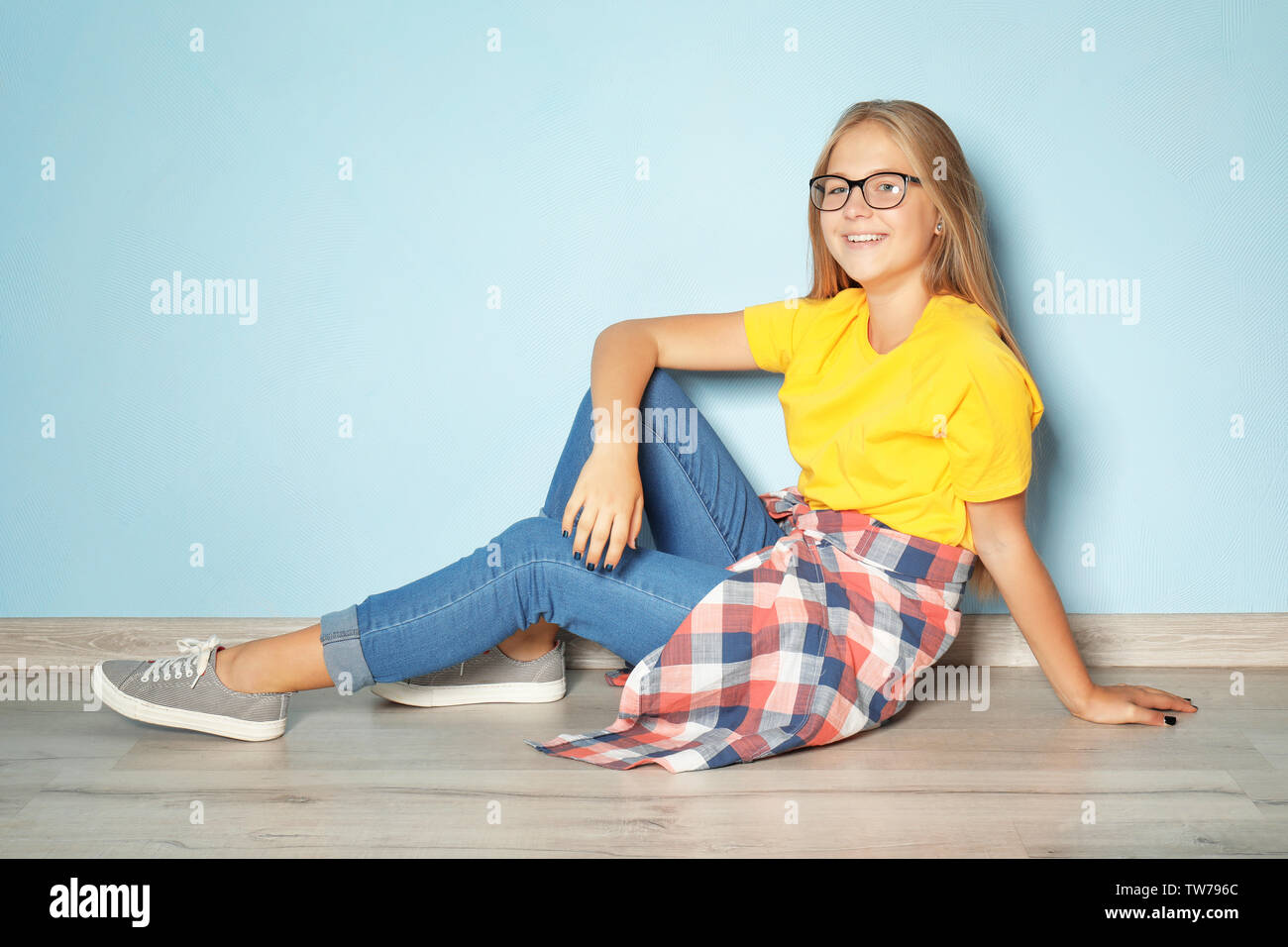 Cute teenager girl sitting on floor near color wall Stock Photo - Alamy