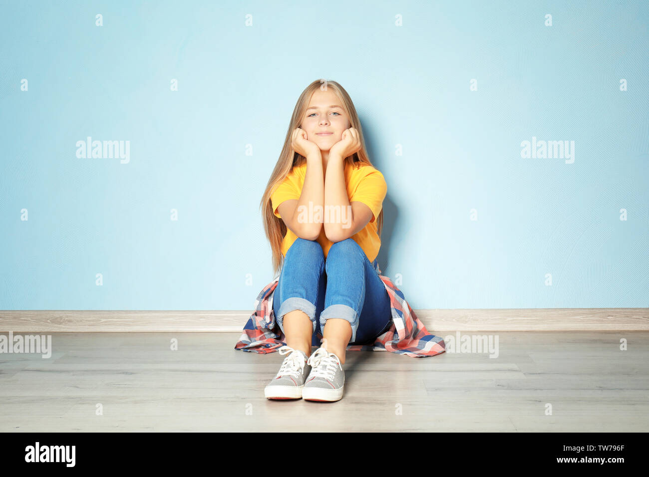 Cute teenager girl sitting on floor near color wall Stock Photo - Alamy