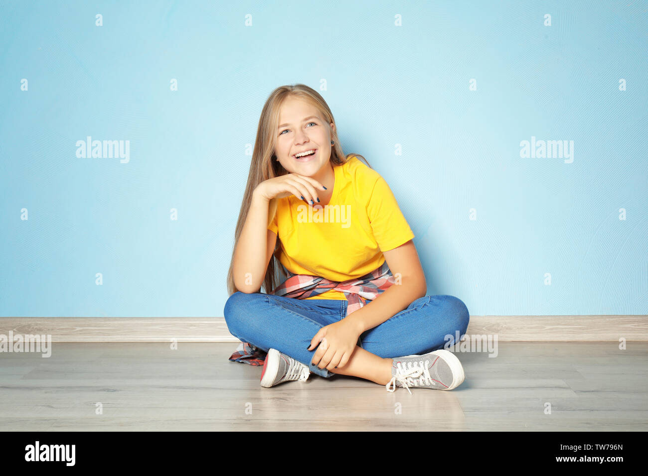 Cute teenager girl sitting on floor near color wall Stock Photo - Alamy