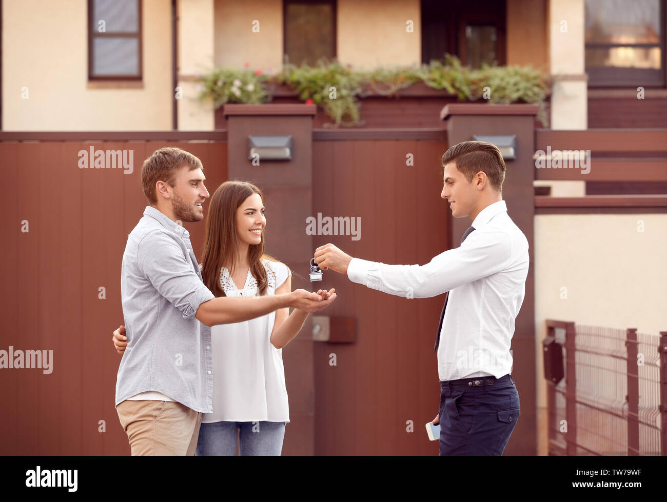 Real estate agent giving key to young couple near house Stock Photo - Alamy