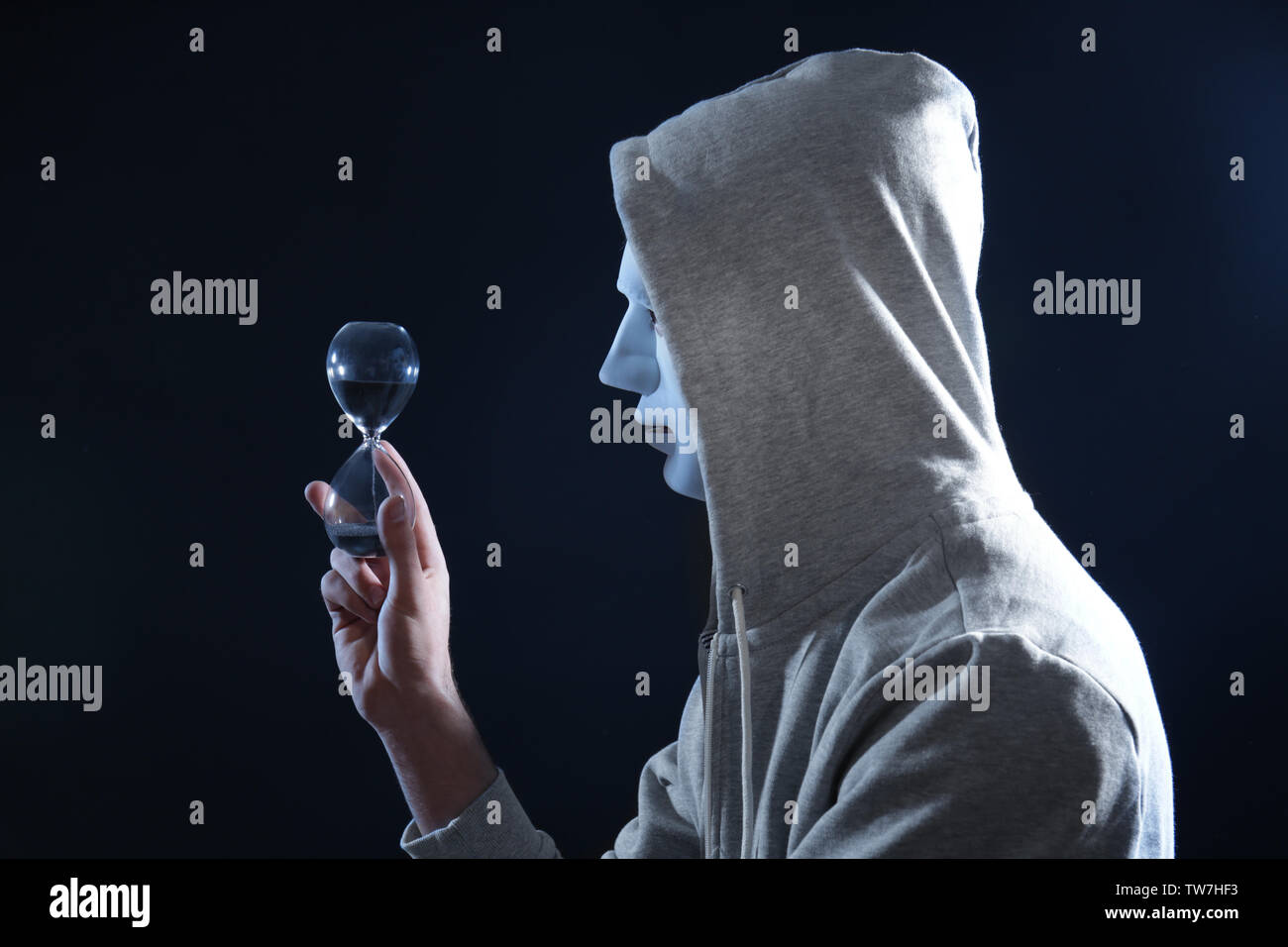 Masked hacker with sand clock in darkness Stock Photo
