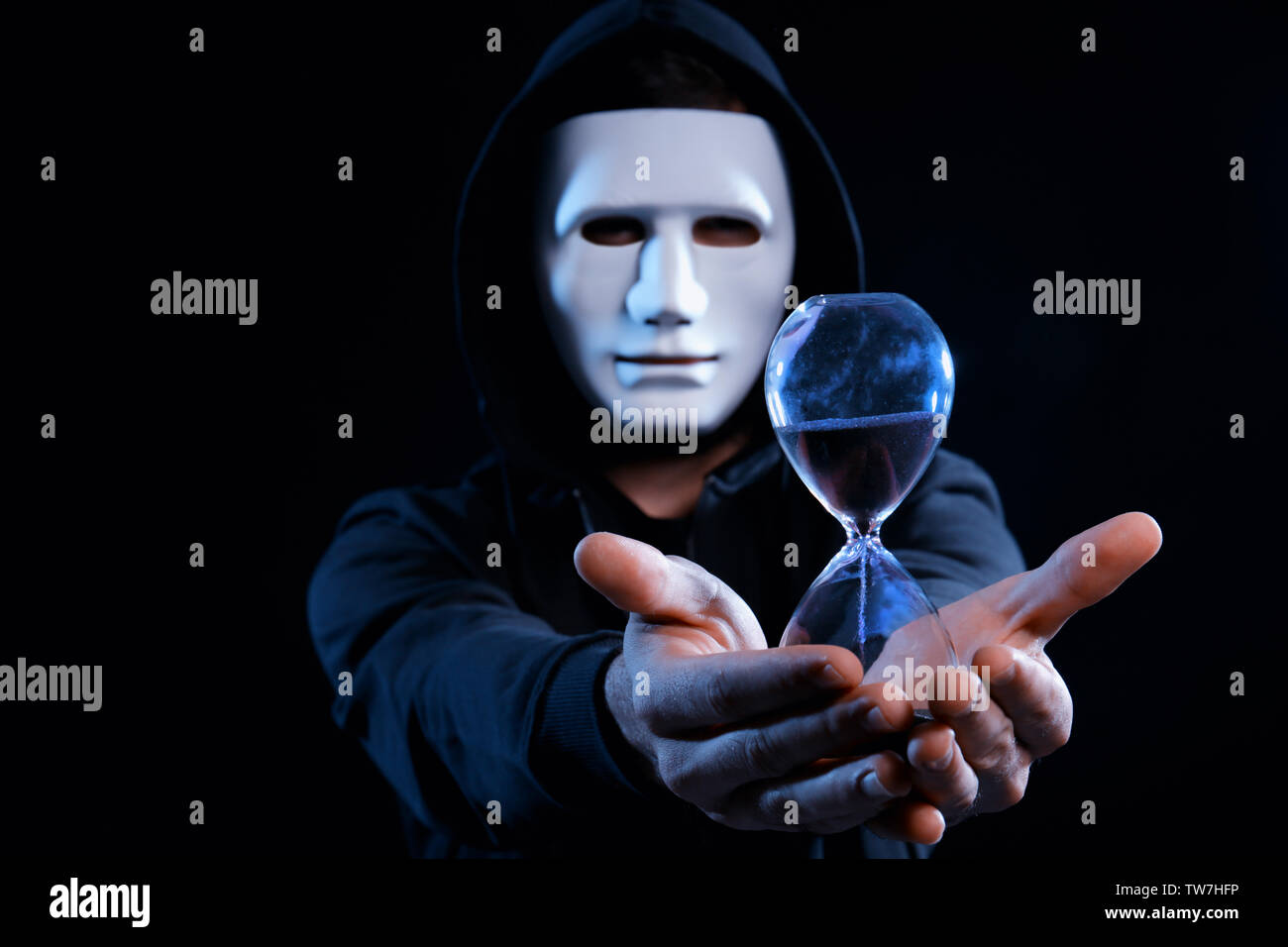 Masked hacker with sand clock in darkness Stock Photo