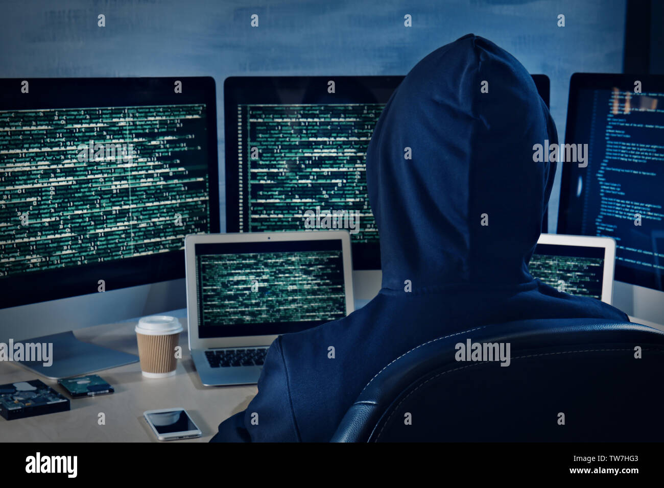 Man in hoodie hacking server at table Stock Photo