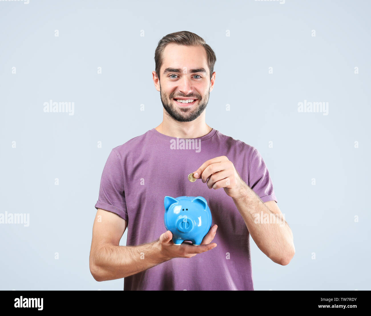 Casual man putting some coins into a piggy bank in living room Stock ...