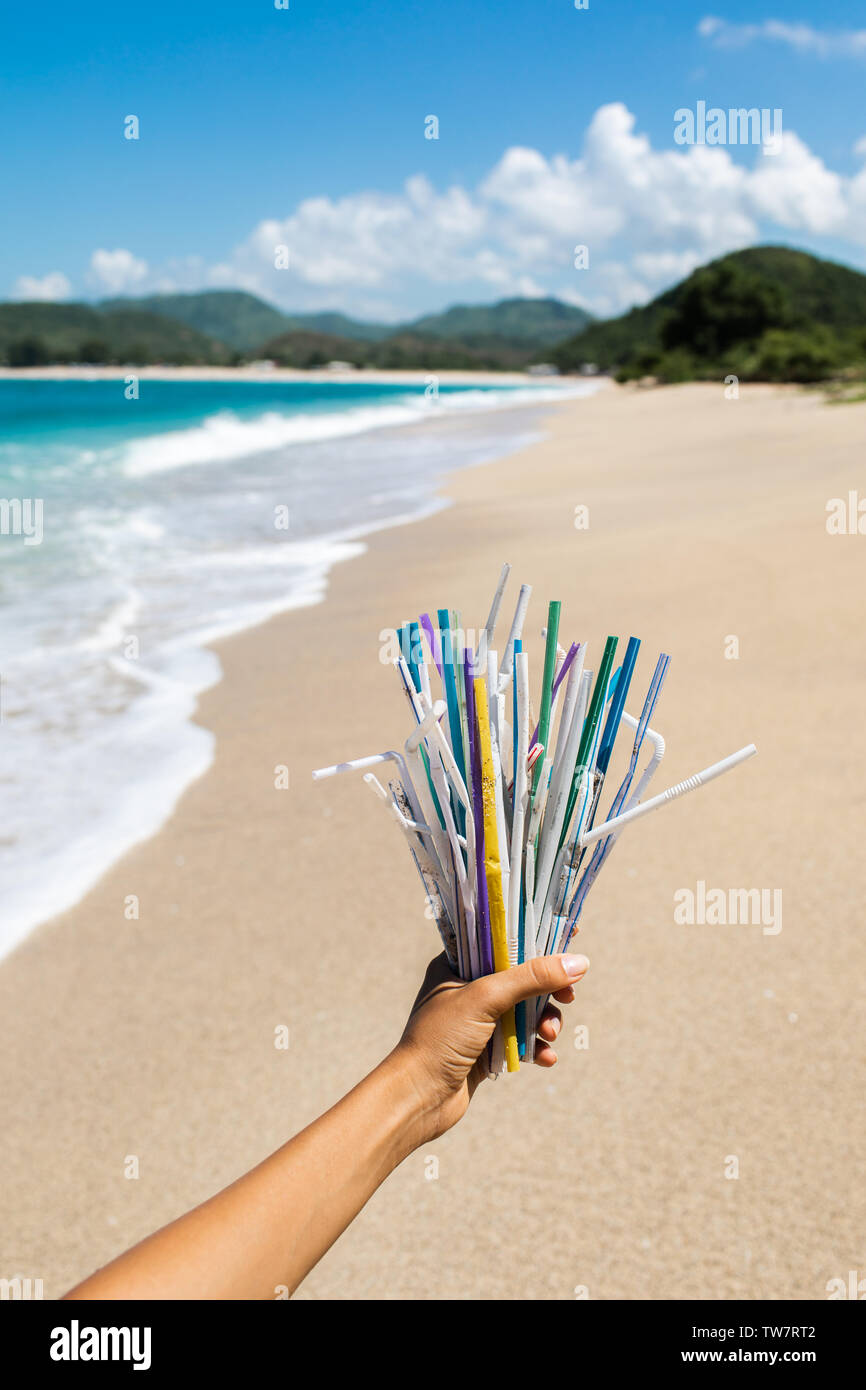 Hand holding heap of used plastic straws on background of clean beach and ocean waves. Plastic ocean pollution, environmental crisis. Say no plastic. Stock Photo