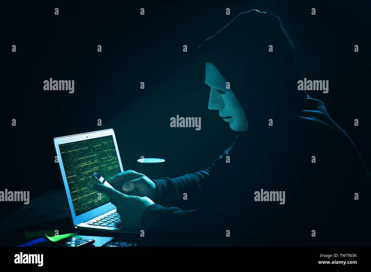 Hacker in mask with laptop and cell phone in dark room Stock Photo - Alamy
