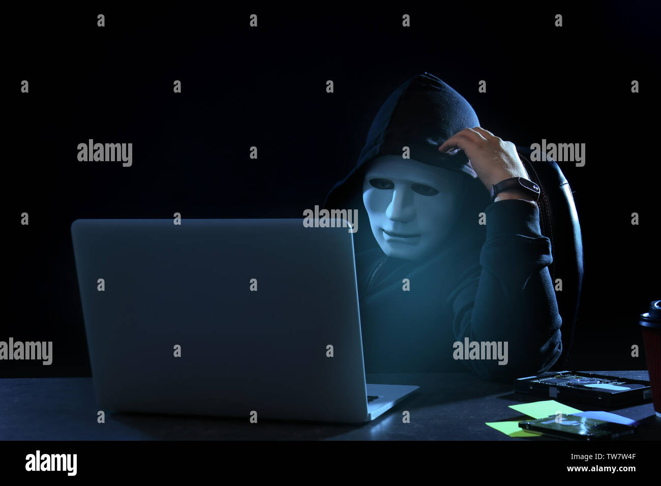 Hacker in mask using laptop in dark room Stock Photo - Alamy