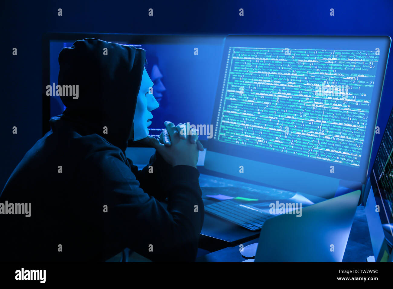 Hacker in mask using computer in dark room Stock Photo - Alamy