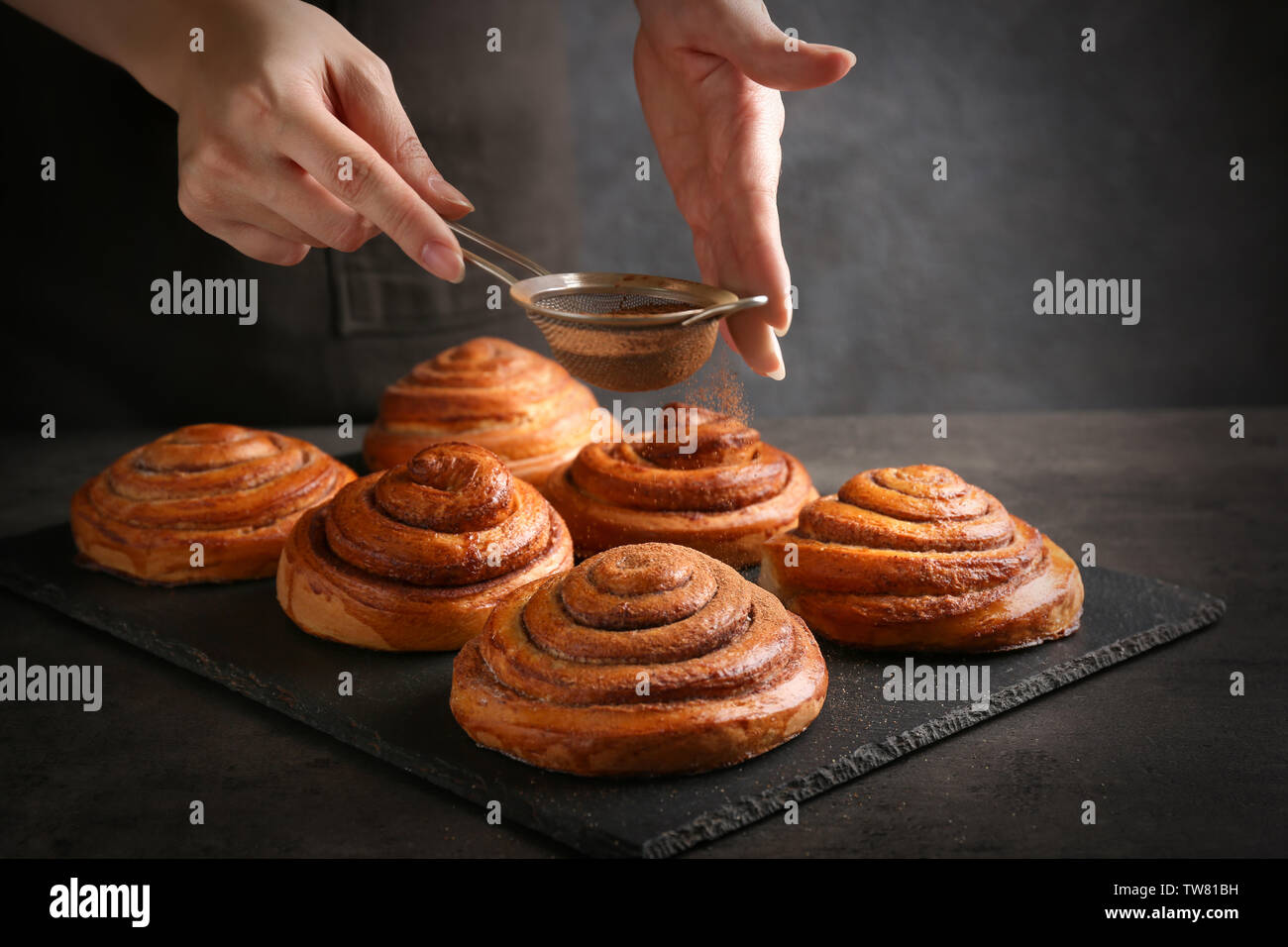 Woman sprinkling sweet rolls with cinnamon on slate plate Stock Photo