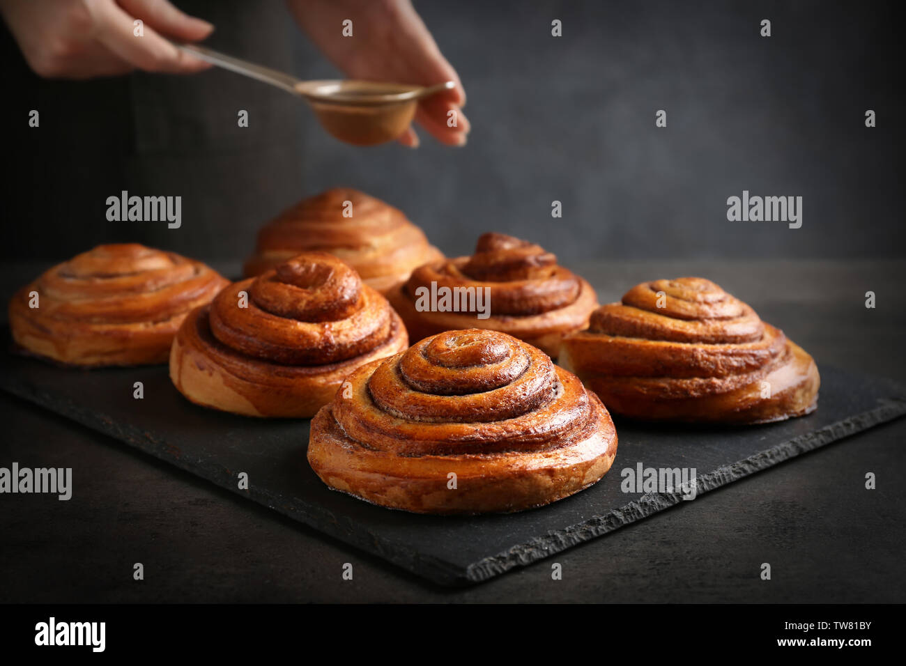 Woman sprinkling sweet rolls with cinnamon on slate plate Stock Photo
