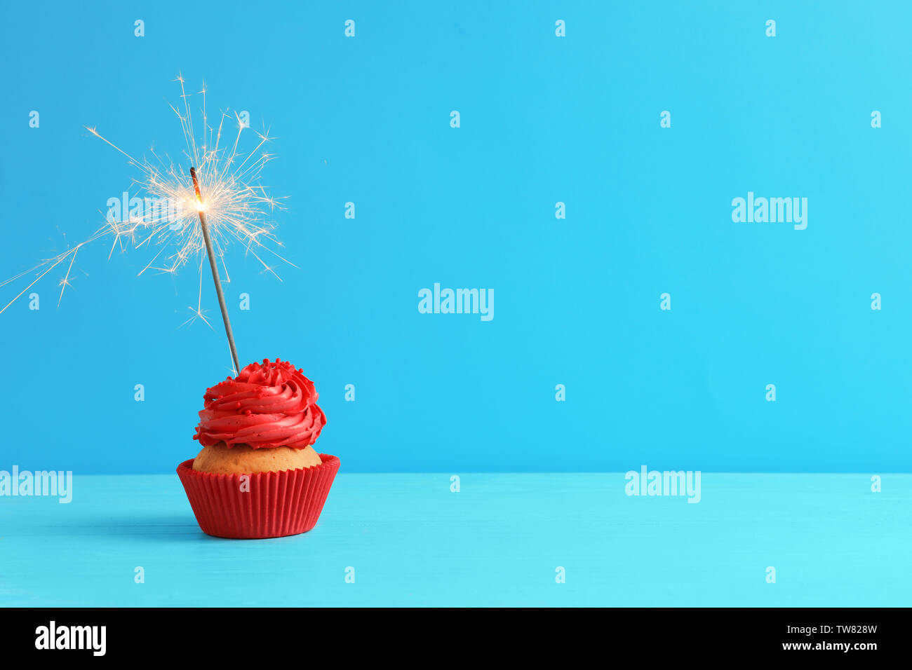 Tasty cupcake with sparkler on table against color background Stock Photo