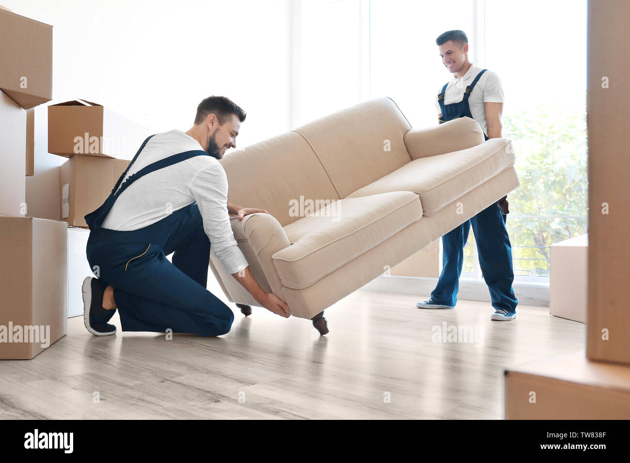 Delivery men moving sofa in room at new home Stock Photo Alamy