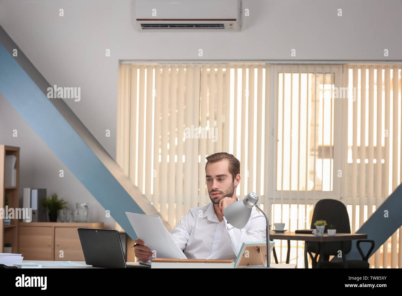 Young man working in office with operating air conditioner Stock Photo