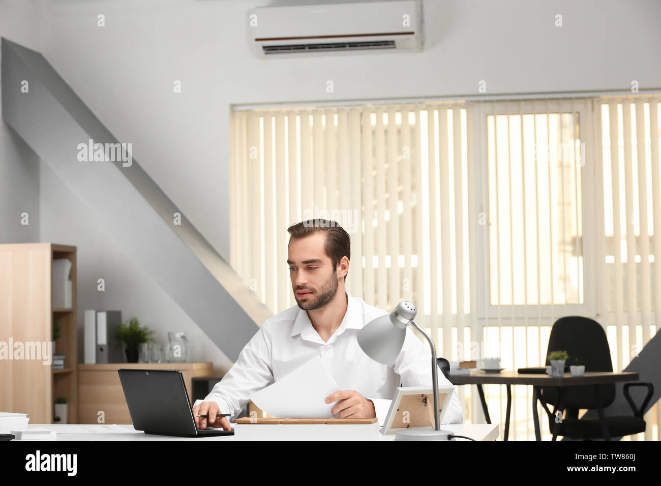 Young man working in office with operating air conditioner Stock Photo