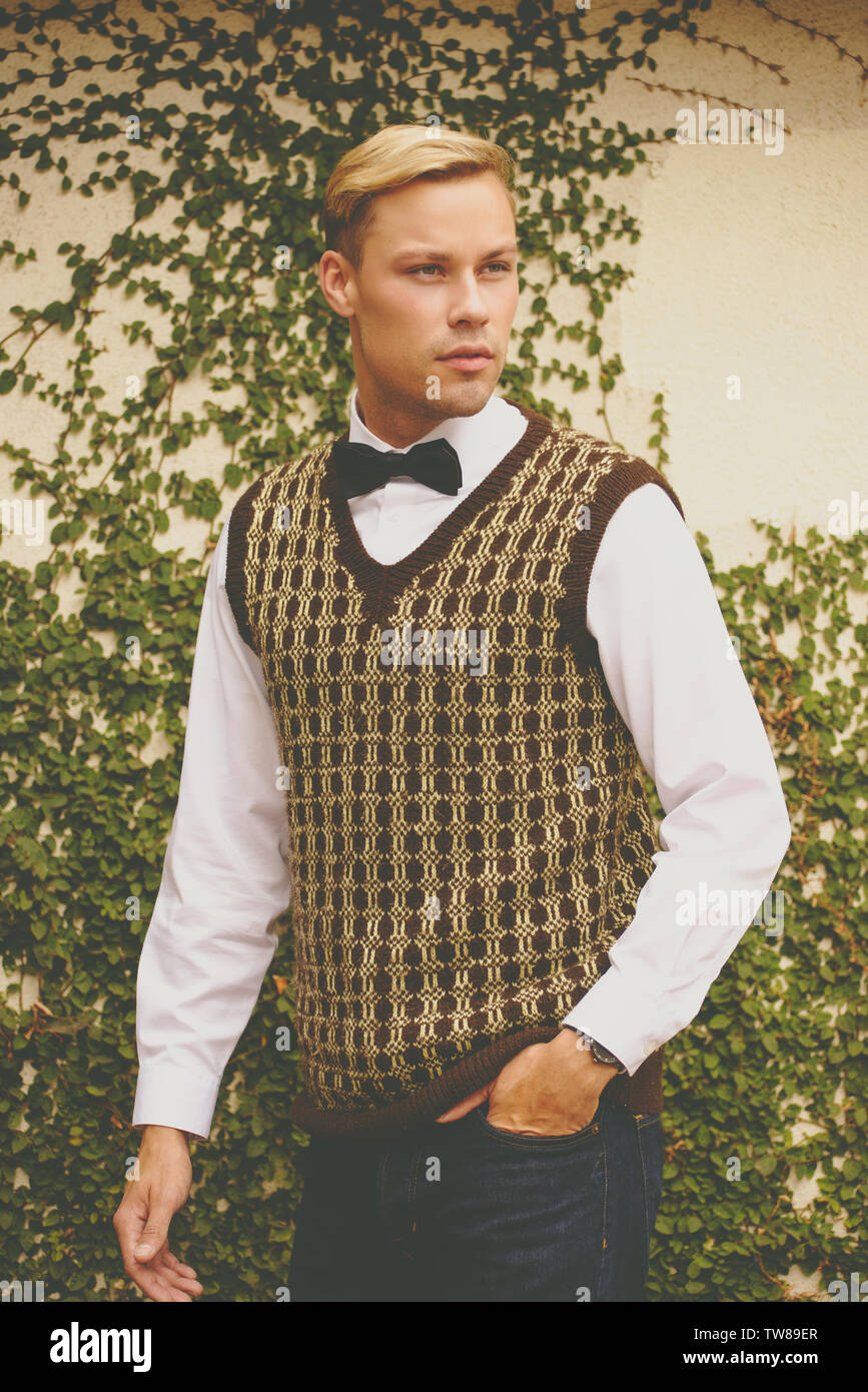 Blonde Caucasian male model modeling vintage 70s clothes outdoor, he wears a bow tie and vest. Stock Photo