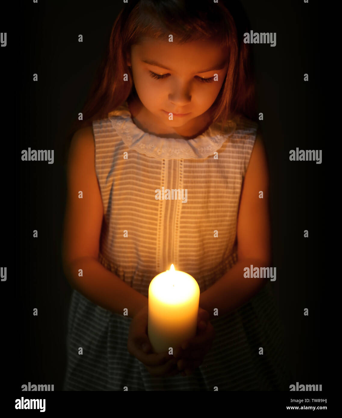 Little girl holding burning candle in darkness Stock Photo Alamy
