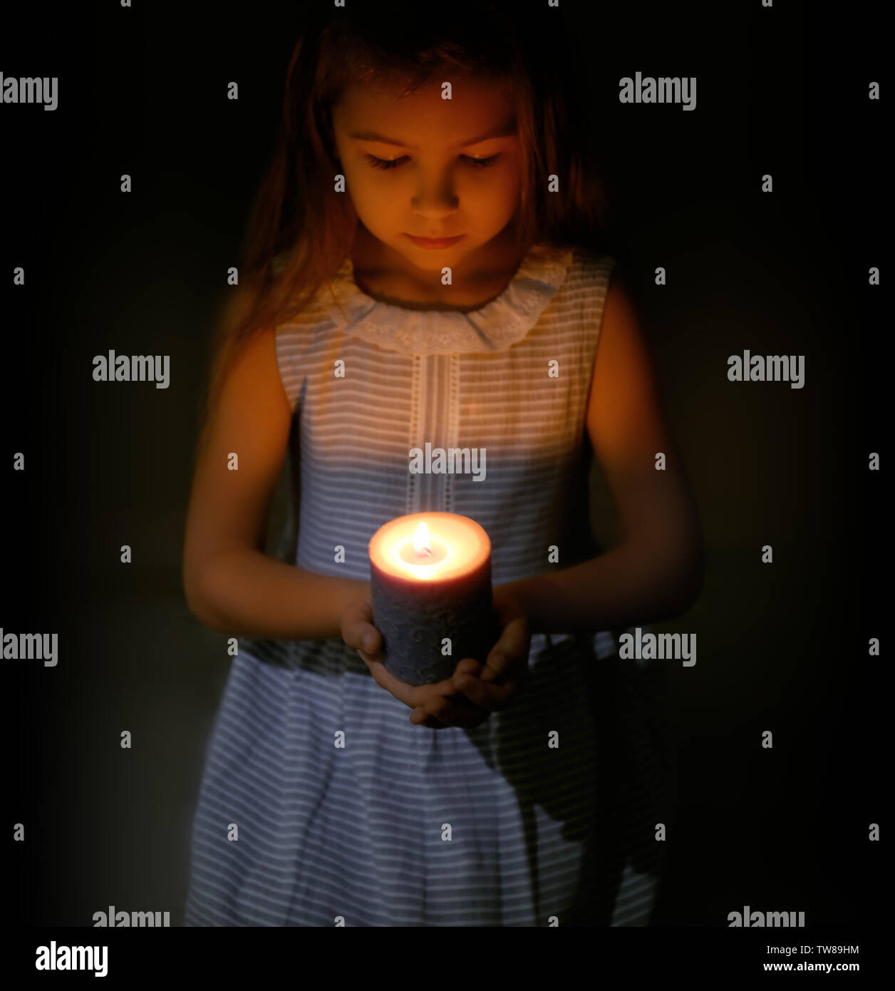 Little girl holding burning candle in darkness Stock Photo Alamy