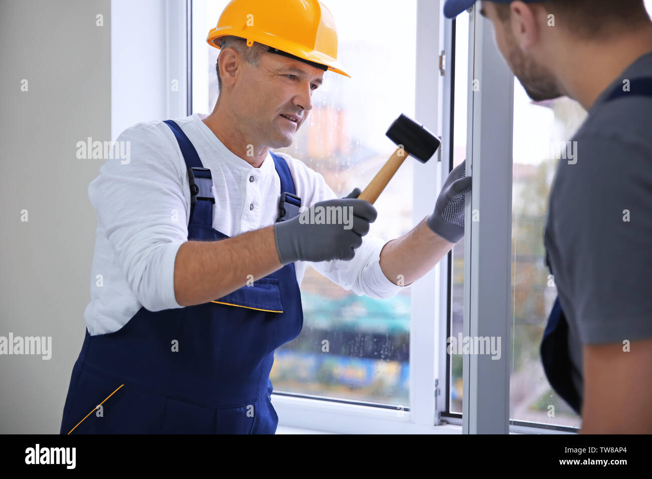 Construction worker with trainee installing window in house Stock Photo