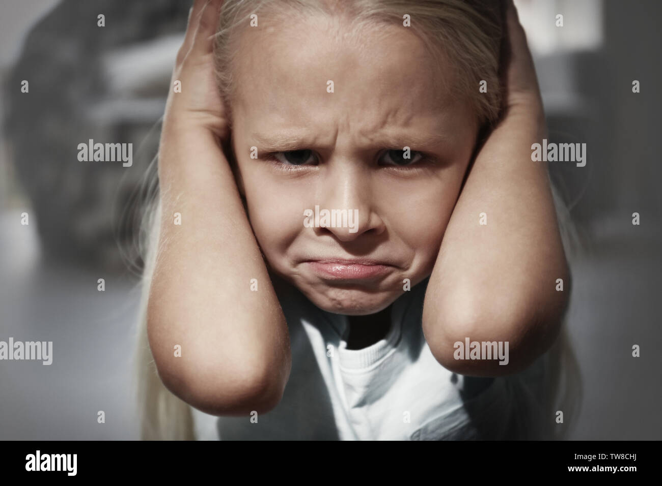 Helpless little girl covering her ears indoors. Child abuse concept