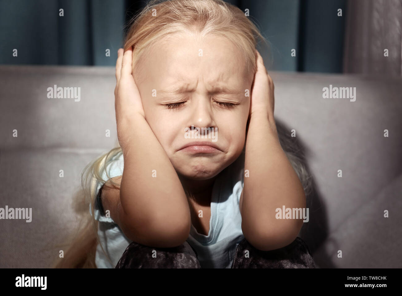 Helpless little girl covering her ears indoors. Child abuse concept