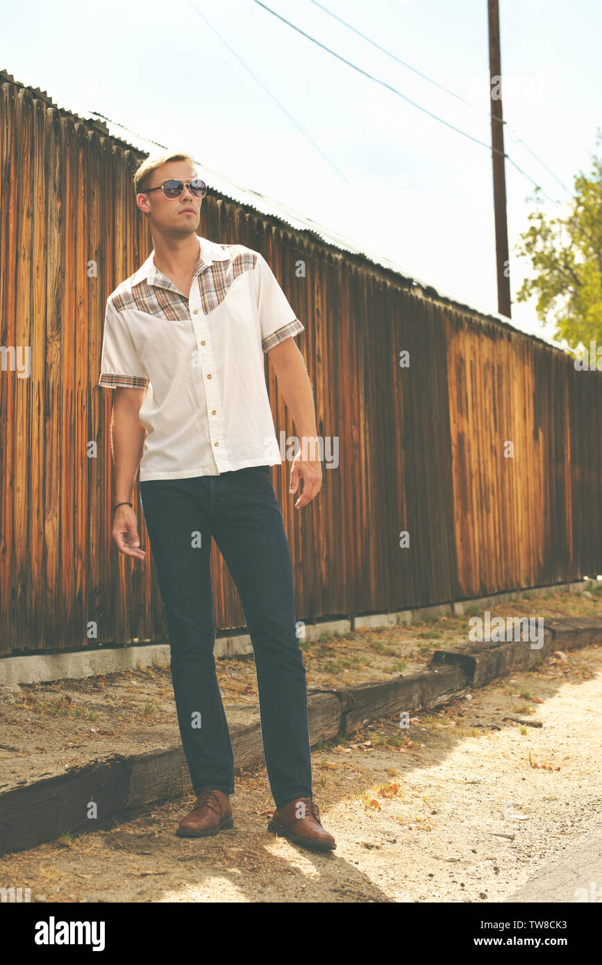A White Caucation model wearing a western shirt posing by wooden fence wearing aviator sunglasses posing outdoor, a fashion portrait. Stock Photo