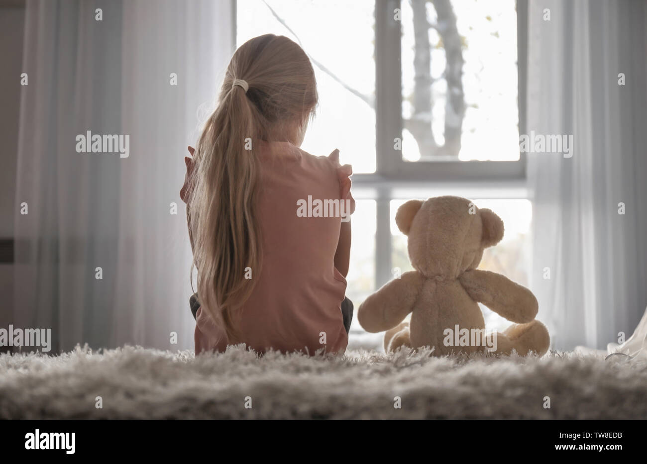 Little girl with teddy bear sitting on floor in room. Autism concept ...