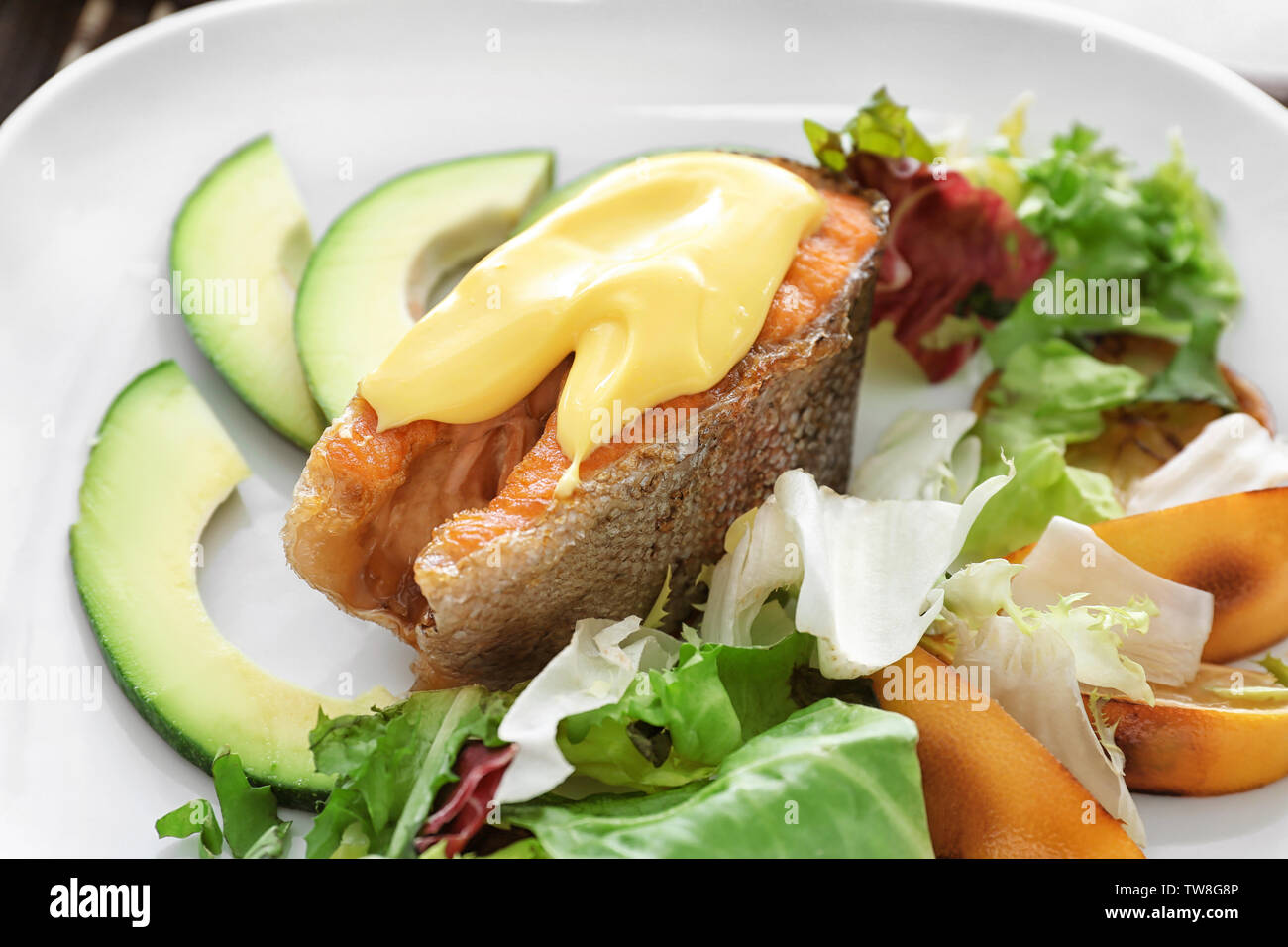 Tasty rainbow trout steak with garnish and sauce on plate, closeup