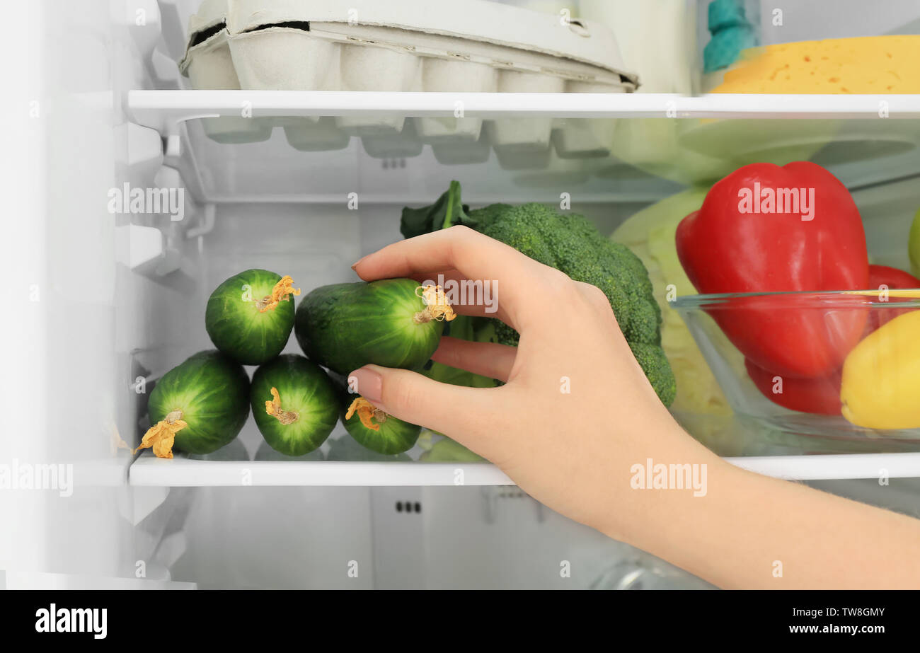 Woman taking cucumber from refrigerator, closeup Stock Photo