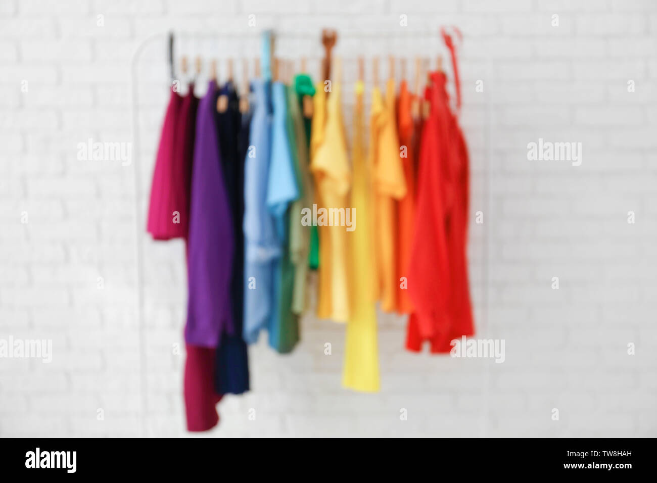 Rack with rainbow clothes near brick wall, blurred view Stock Photo - Alamy
